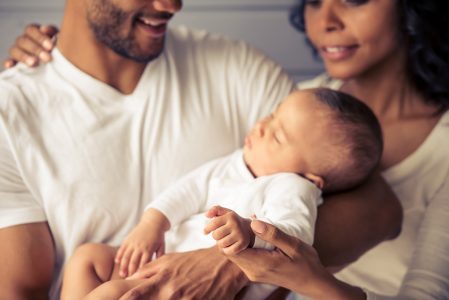 Cropped image of beautiful young Afro American parents smiling while little baby is sleeping in dad's arms
